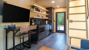 A modern kitchen with a built-in oven, a coffee machine, and a sink. There is a bar area with stools and a television mounted on the wall. - Scandinavian Treetop Bliss @ Terralodge (Monteagle)