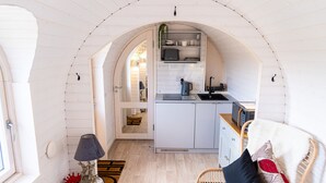 Et buet køkken med hvide skabe, en mikrobølgeovn og en elkedel. Der er en fletstol med et plaide og puder.