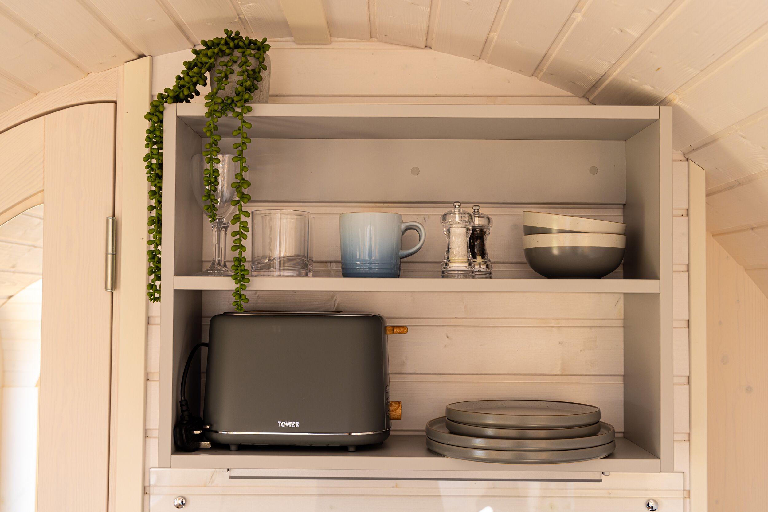 A kitchen with a built-in toaster, shelves with glassware, a blue mug, and a salt and pepper set.