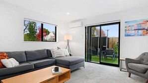 A modern living room with a grey sofa, a wooden coffee table, and a sliding glass door leading to an outdoor area. - Central Convenience on Armagh (Christchurch)