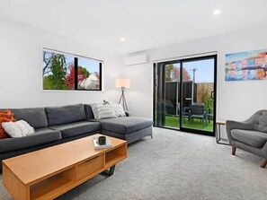 A modern living room with a grey sofa, a wooden coffee table, and a sliding glass door leading to an outdoor area.
