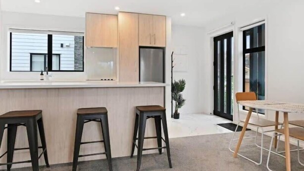 A modern kitchen with a bar area, wooden cabinets, and a dining table with stools. - Central Convenience on Armagh (Christchurch)