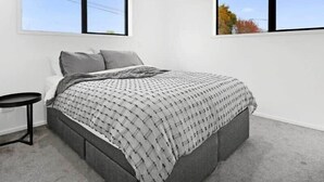 A bedroom with a bed, two windows, a bedside table, and a carpeted floor. - Central Convenience on Armagh (Christchurch)