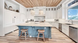 Uma cozinha moderna com armários brancos, uma ilha azul, piso de madeira e luminárias pendentes.