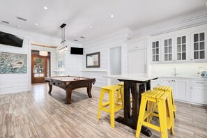 A spacious room with a pool table, yellow stools, and a bar area.