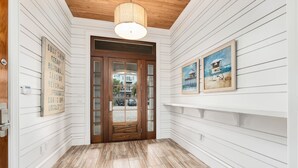 Um corredor com painéis brancos, uma porta de madeira e piso ladrilhado.