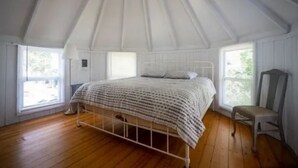A bedroom with a white canopy bed, wooden flooring, and a chair.