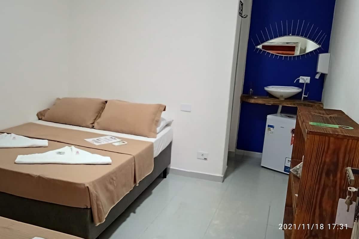 A hotel room with a bed, a wooden dresser, a sink, and a mirror.