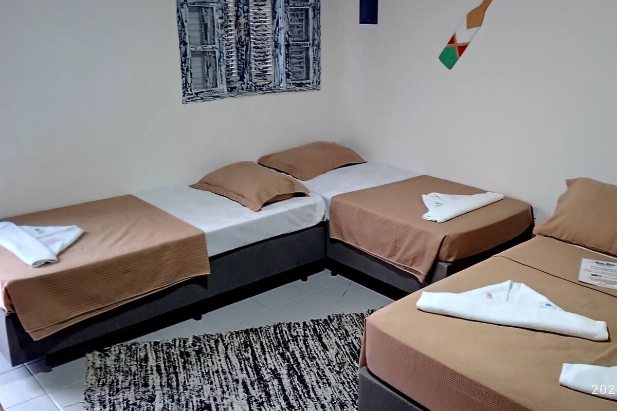 A hotel room with two single beds and one double bed, each with brown bedding and white towels. There is a black and white patterned rug on the floor, and a small table with a phone and a piece of paper.