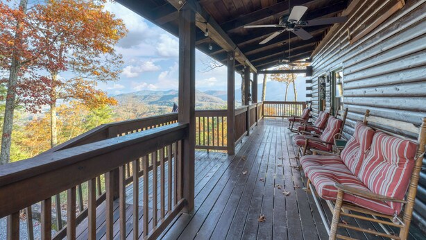 Terraza de madera con sofá y sillones, con vista a un paisaje montañoso con follaje otoñal.