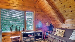 Un interior cálido de cabaña con paredes de madera, un sofá escocés, una silla de madera y una estantería.