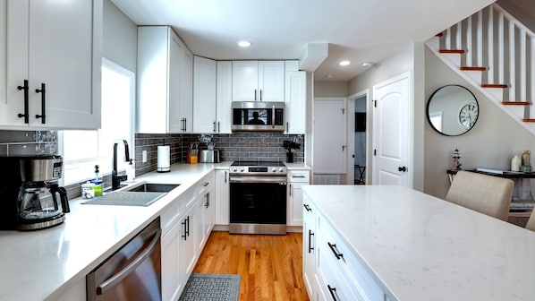 A modern kitchen with white cabinetry, stainless steel appliances, and a wooden floor.