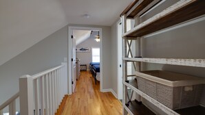 A narrow hallway with wooden flooring, white railings, and a staircase. There are two beds in the background, a ceiling fan, and a window with blinds. - Private Heated Pool - 1 Block from the Beach! (Tybee Island)