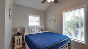 A bedroom with a bed, a nightstand, a lamp, a window with blinds, and a ceiling fan.