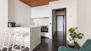 A modern kitchen with white cabinets, a marble island, and two white bar stools. - Riverview Studio in Historical Heart of Antwerp (Antwerpen)