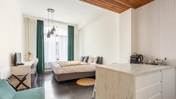 A modern bedroom with a bed, a desk, and a kitchenette. - Riverview Studio in Historical Heart of Antwerp (Antwerpen)