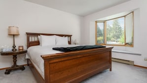 A bedroom with a wooden bed, a bedside table with a lamp, and a window with blinds. - Swansea Serene | Indoor Fireplace | 5 Min to Beach (Windermere)