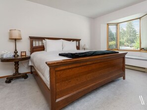 A bedroom with a wooden bed, a bedside table with a lamp, and a window with blinds.