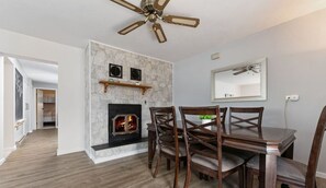 A dining area with a fireplace, wooden chairs, and a ceiling fan.