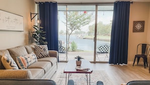 A living room with a sofa, two armchairs, a coffee table, and a view of a body of water through large glass doors. - Lake Conroe Retreat – Relaxing Lake Views - Fish & Swim - Ground Floor (Montgomery)