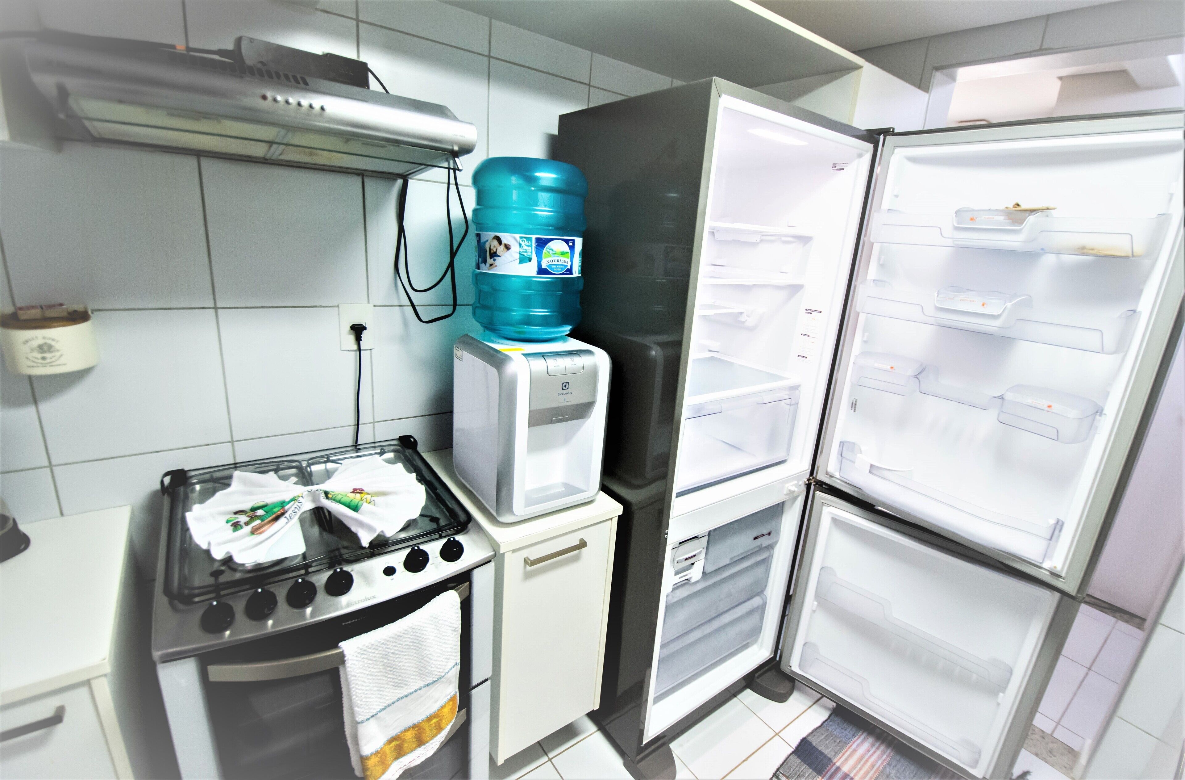 A compact kitchen with a stove, a water dispenser, and two refrigerators.