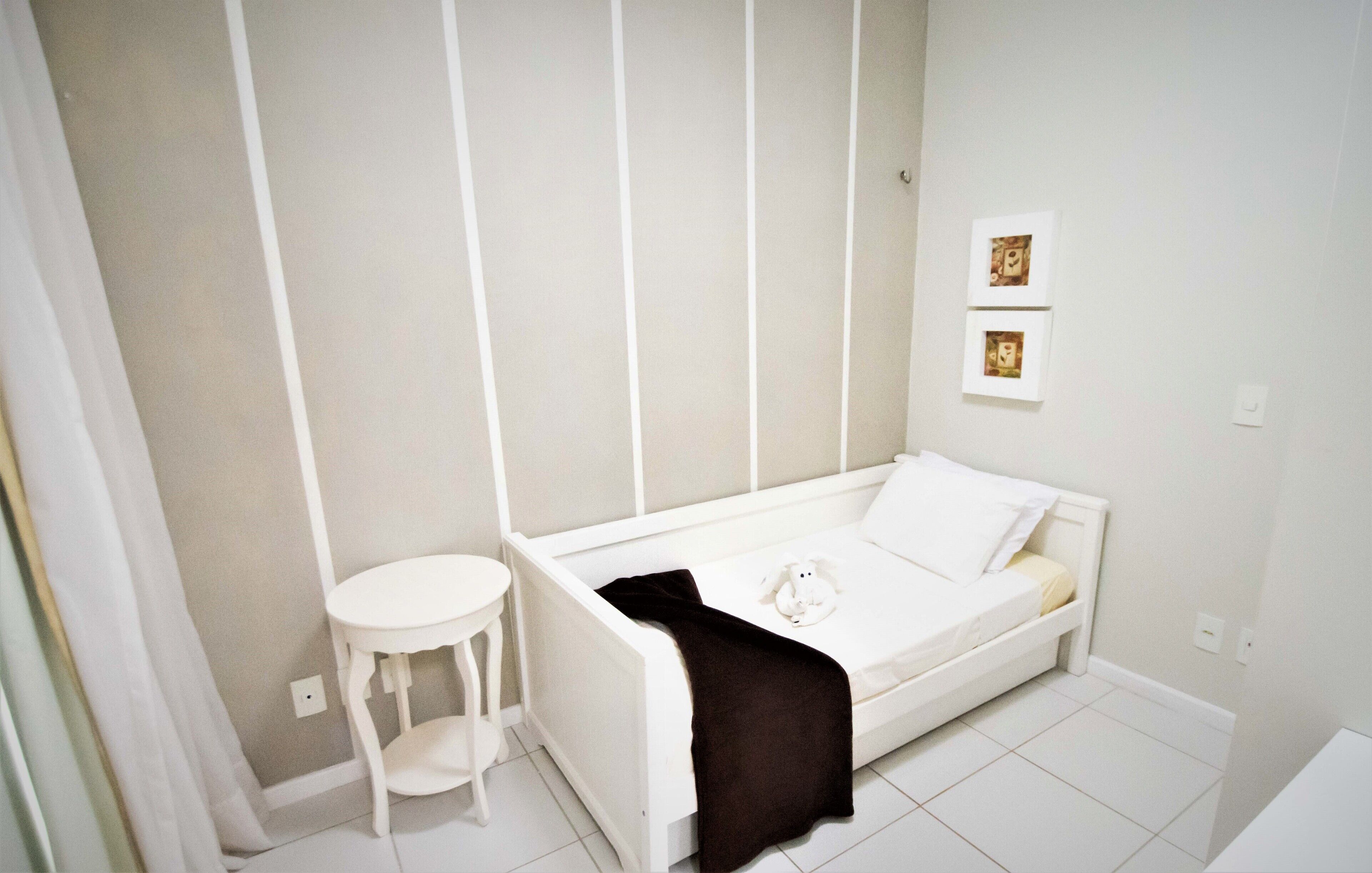 A small, white, single-bed room with a bedside table and a wall-mounted picture.