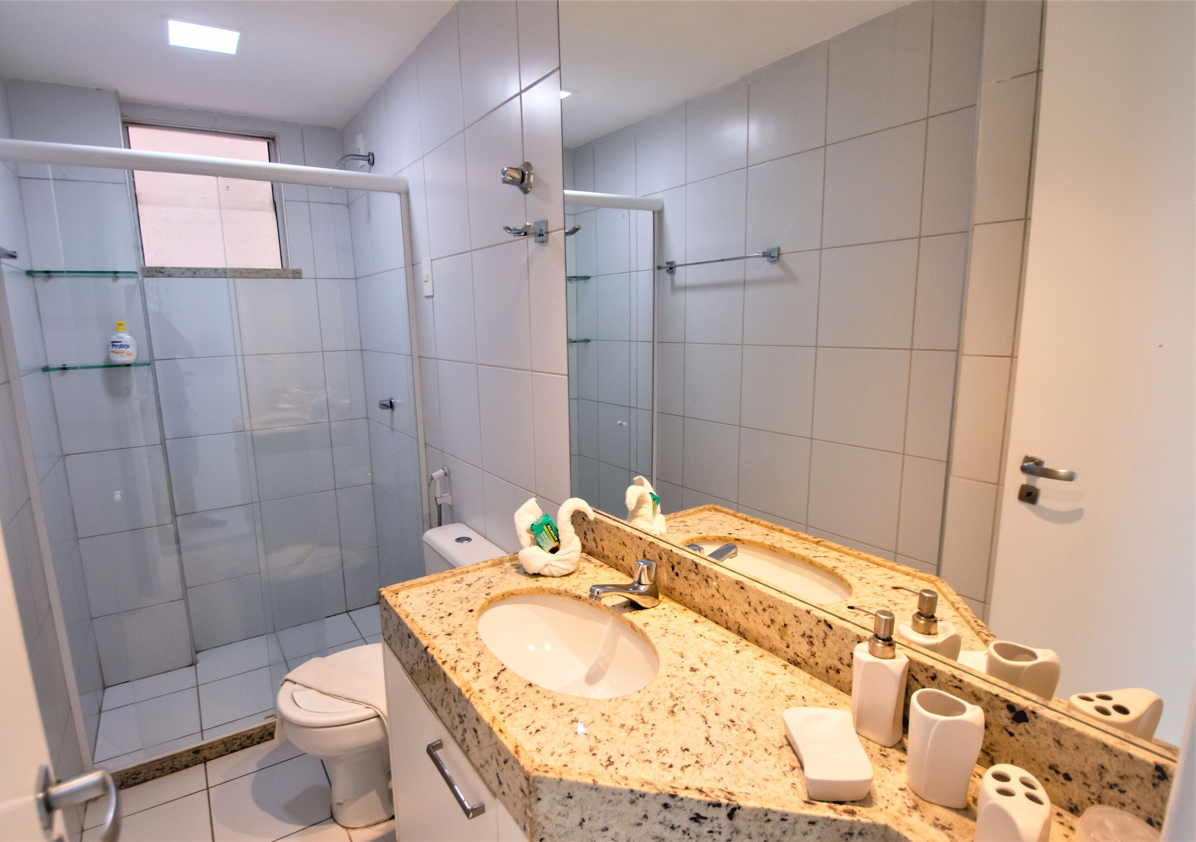 A modern bathroom with a granite countertop sink, a large mirror, and a glass shower enclosure.