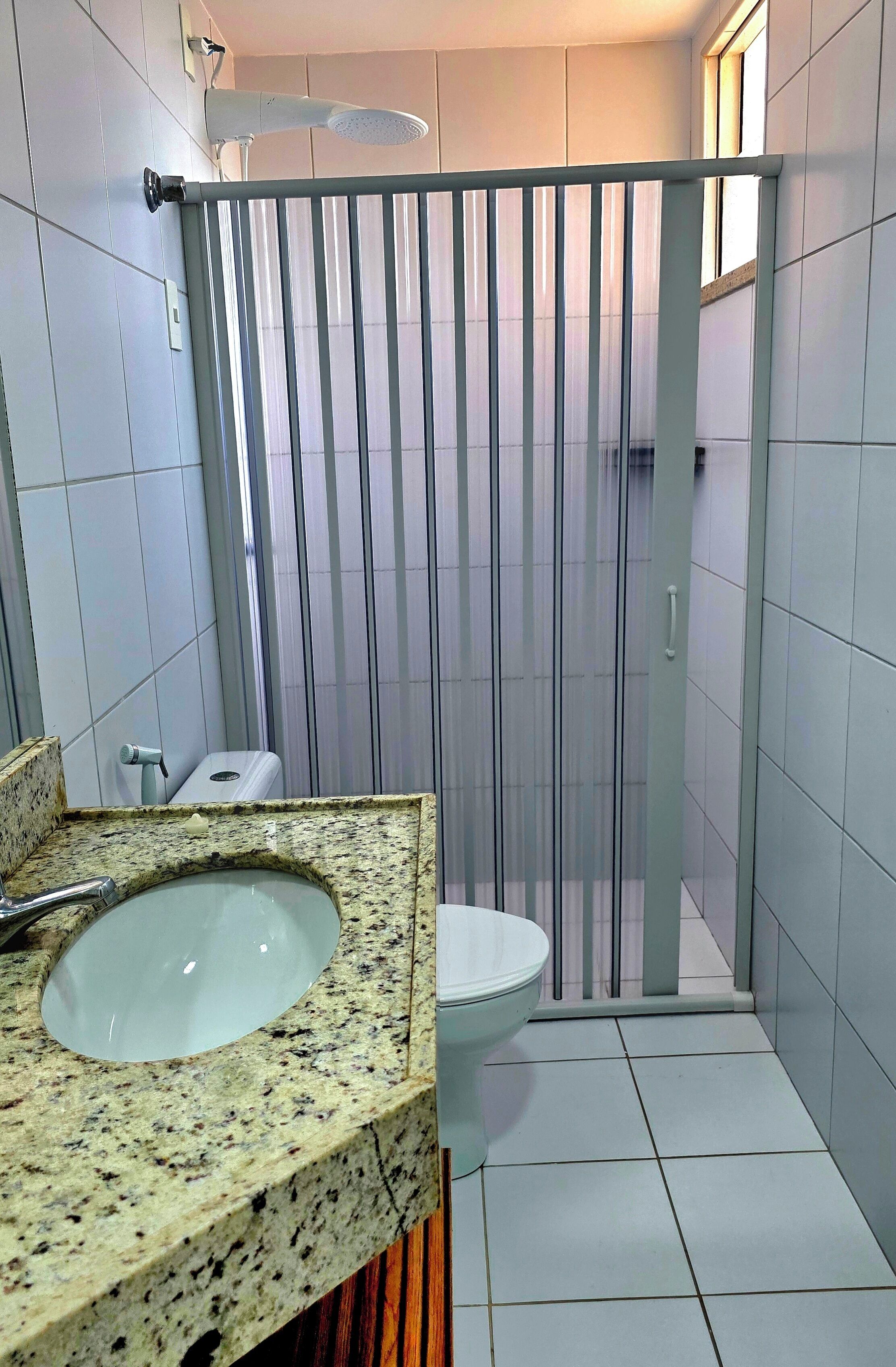 A bathroom with a granite countertop, a sink, a toilet, and a shower enclosure with a glass door.