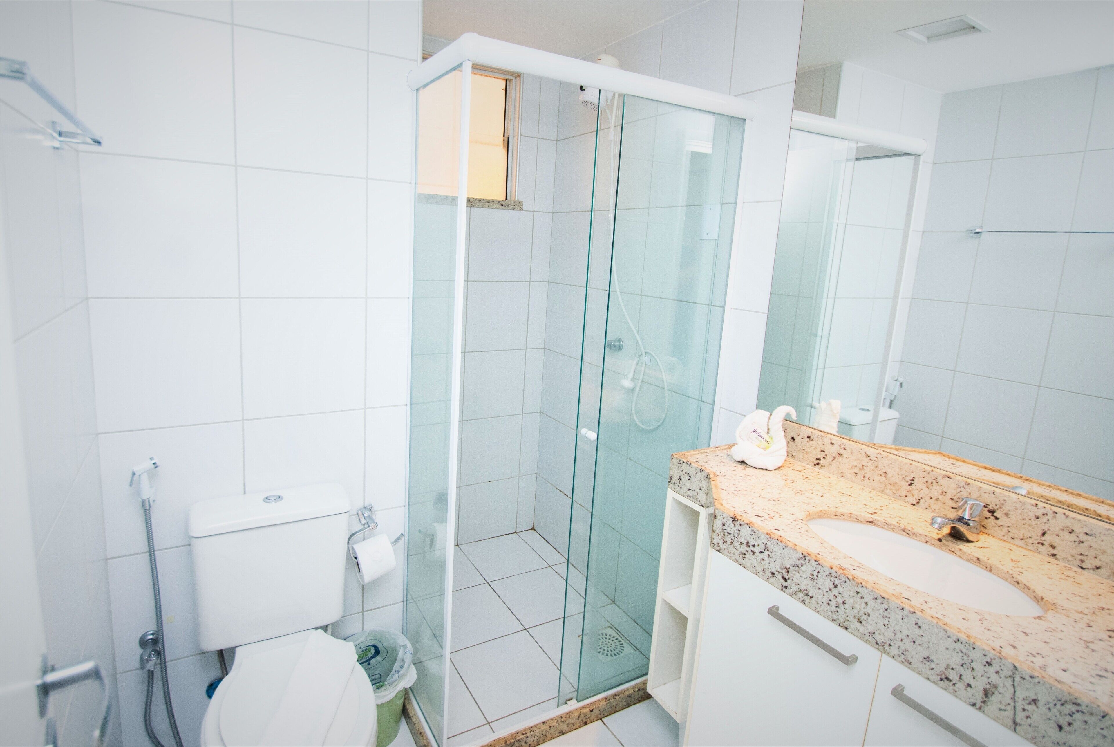 Ein modernes Badezimmer mit einer gläsernen Duschkabine, einem Waschtisch aus Granit und weiß gefliesten Wänden.