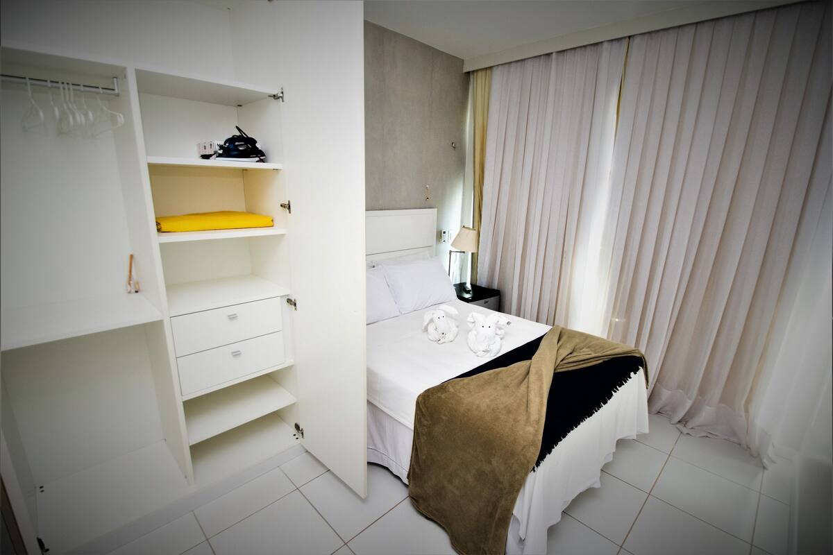 Ein Schlafzimmer mit einem Bett, einem Kleiderschrank, einem Nachttisch und einem Fenster mit Vorhängen.