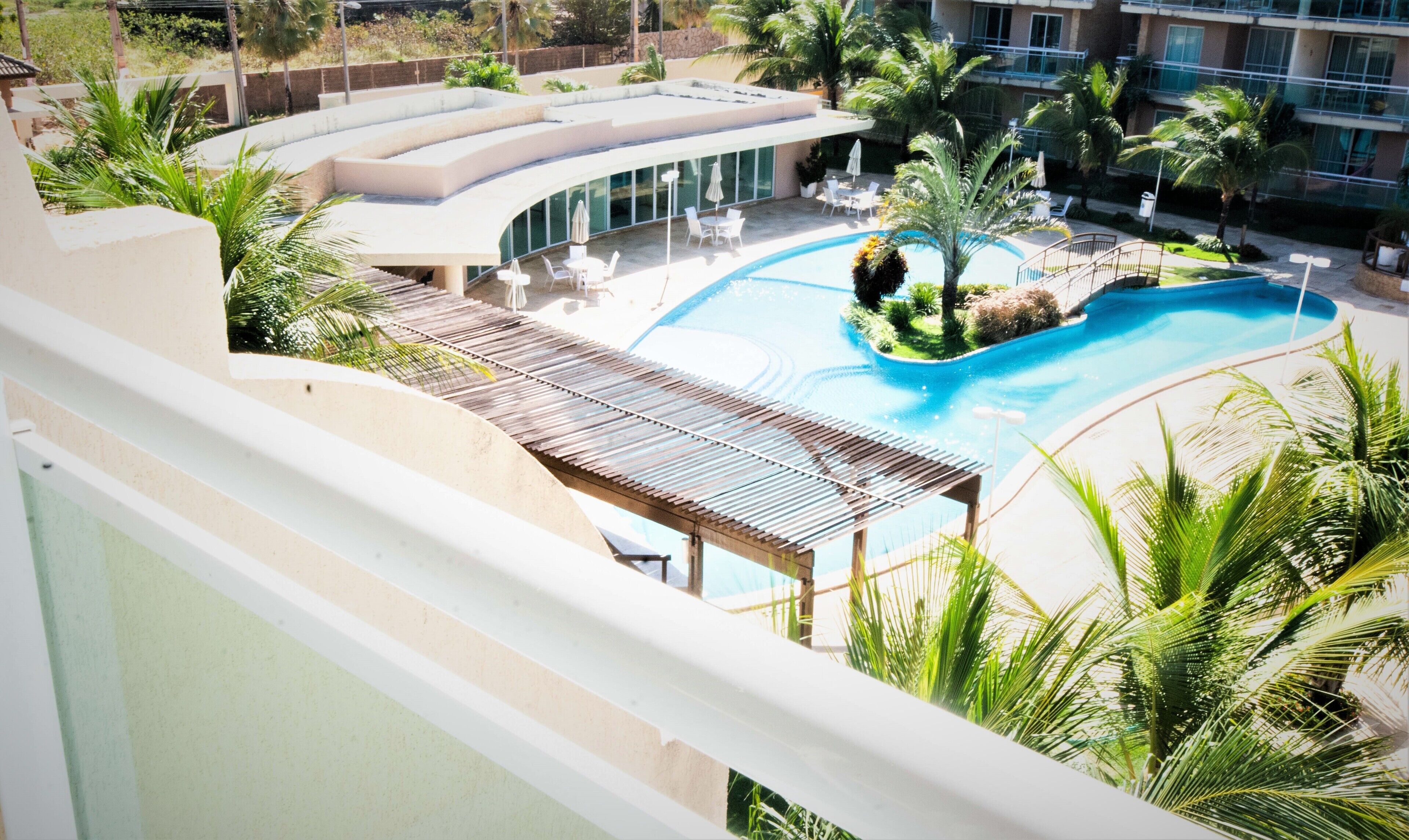 Un resort con una gran piscina, palmeras y un edificio moderno de techo curvo.