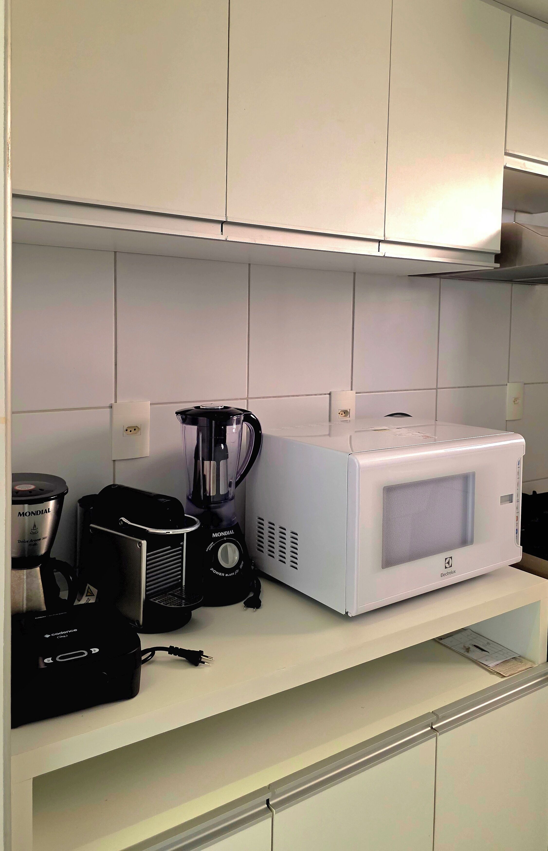 Cuina amb armaris blancs, una cafetera, un batedor i un microones a la superfície.