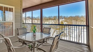 En overdækket udendørs terrasse med et bord og stole, store vinduer og udsigt til et sneklædt landskab.