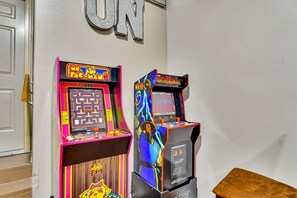 Two arcade machines, one labeled 'Pac-Man' and the other 'Mortal Kombat', in a room with a wooden floor and a white door.