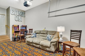 Ein Zimmer mit einem beigefarbenen Sofa, zwei Sesseln, einer Lampe und Spielautomaten.