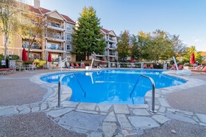 A swimming pool with a stone border, surrounded by lounge chairs and umbrellas, with multi-story buildings in the background. - No Stairs! Condo Minutes from Branson Strip! (Branson)