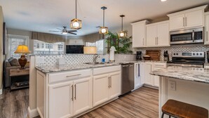 Una cocina amplia con armarios blancos, una isla central, electrodomésticos de acero inoxidable e iluminación colgante.