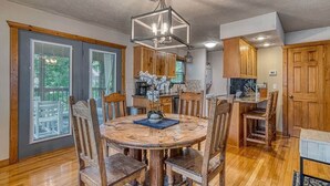 Un coin repas avec une table ronde en bois et des chaises, un lustre et des meubles de rangement en bois.