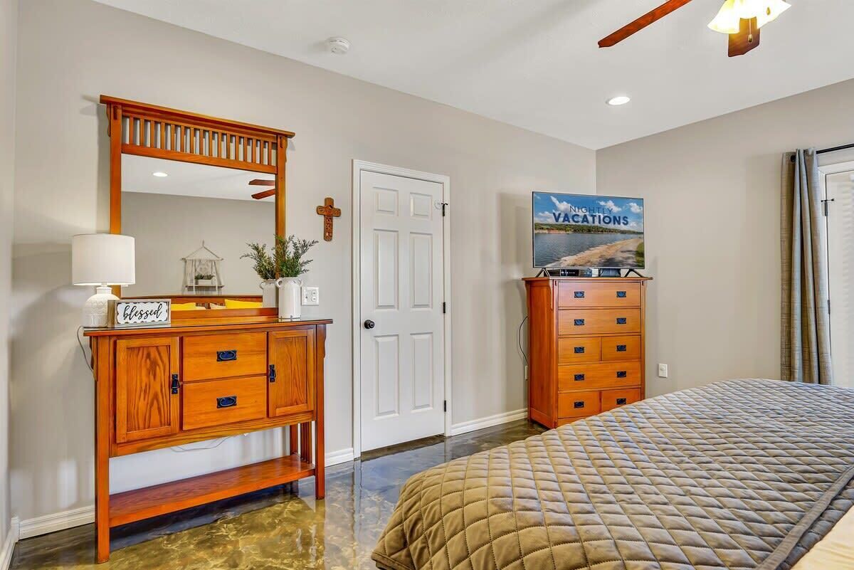 A bedroom with a bed, a wooden dresser, a mirror, a door, and a poster on the wall.