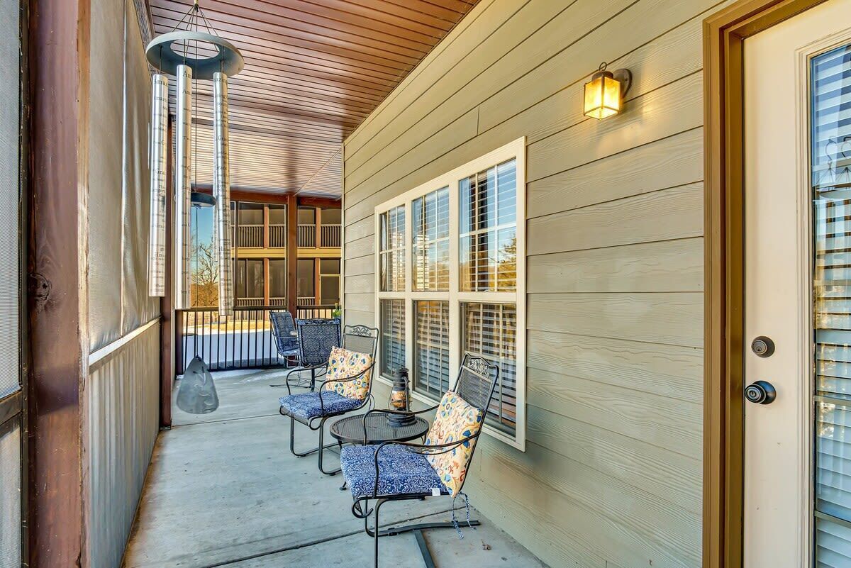 A covered porch with outdoor seating, a decorative wind chime, and a wall-mounted light fixture.