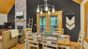 A cozy dining area with a wooden table and chairs, a stone wall, and a television in the background. - Modern Lodge, 3 Miles from Silver Dollar City! (Reeds Spring)