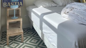 Un dormitorio con cama, una silla de madera pequeña, un cartel en la pared y baldosas de suelo estampadas.