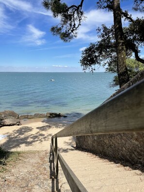 Una playa con un paseo de madera que lleva al agua, cielos despejados y una vista distante del mar.
