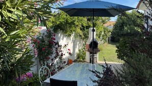 Un patio con una mesa y sillas, un horno de pizza y una pérgola con un paraguas azul.