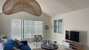Una sala de estar moderna con un sofá azul, una mesa de centro redonda, un televisor y una lámpara colgante grande de fibras naturales.