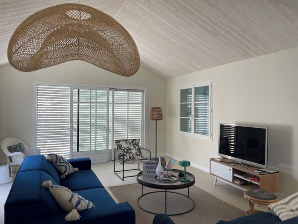 Una sala de estar moderna con un sofá azul, una mesa de centro redonda, un televisor y una lámpara colgante grande de fibras naturales.