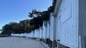 Una hilera de cabañas blancas en la playa, con arena y árboles al fondo.