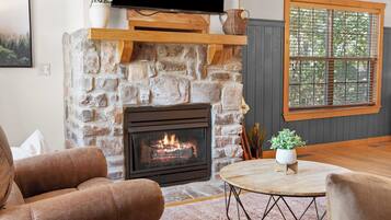 A living room with a stone fireplace, a television mounted above it, and a window with blinds.