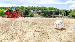 A sandy beach volleyball court with a net, a volleyball, and a red play structure. - Perfect Cabin Retreat! Close to Silver Dollar City (Branson West)