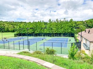 Canchas de tenis múltiples, rodeadas por una cerca, y un edificio con fachada de piedra al fondo.